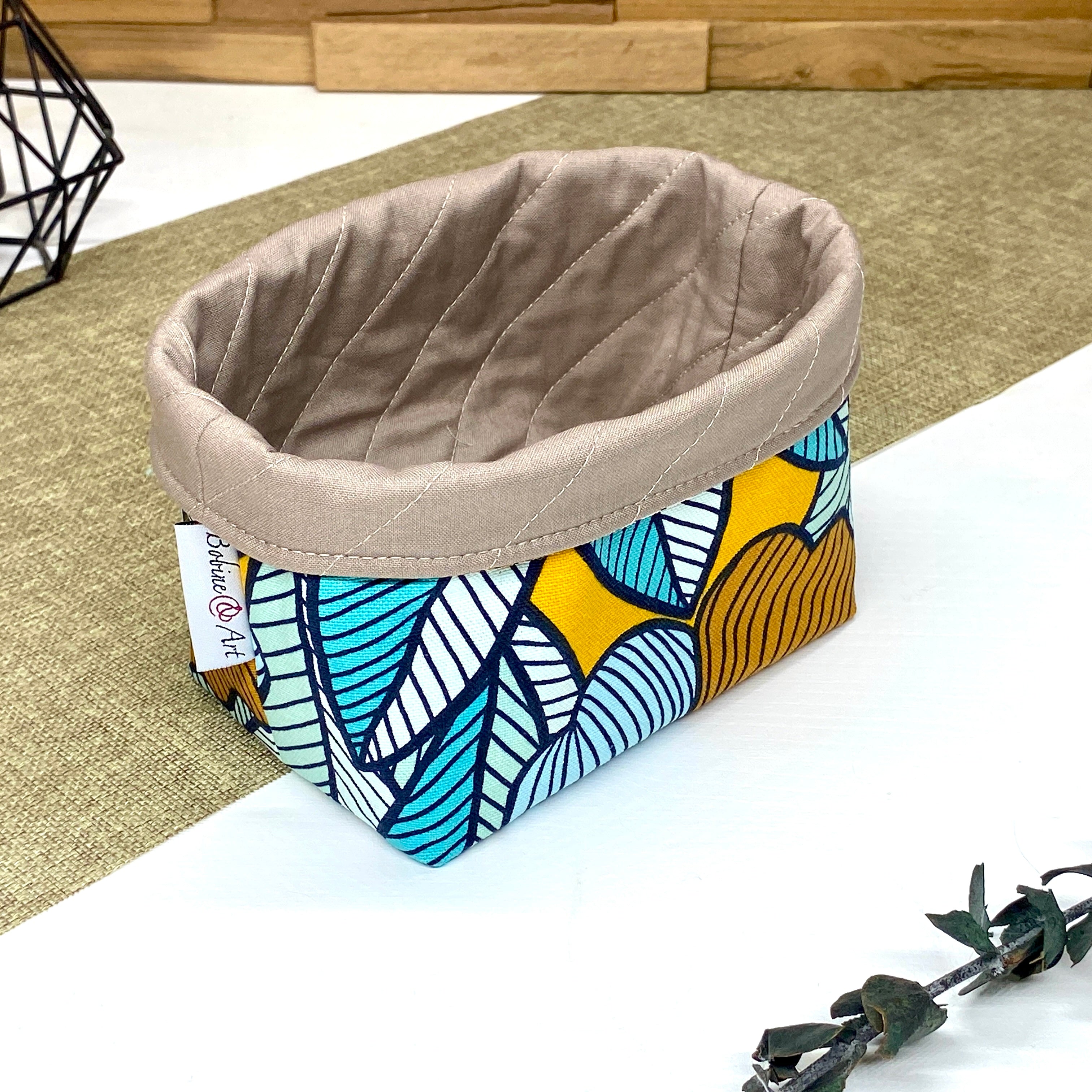 Panière de rangement textile artisanale à motif feuilles graphiques bleu pétrole, bleu ciel et jaune moutarde, idéale pour organiser accessoires, cosmétiques ou lingettes lavables.