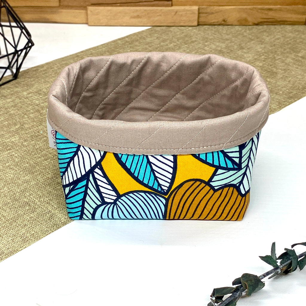 Panière de rangement textile artisanale à motif feuilles bleu pétrole, turquoise et jaune moutarde, idéale pour organiser accessoires, cosmétiques ou lingettes lavables.
