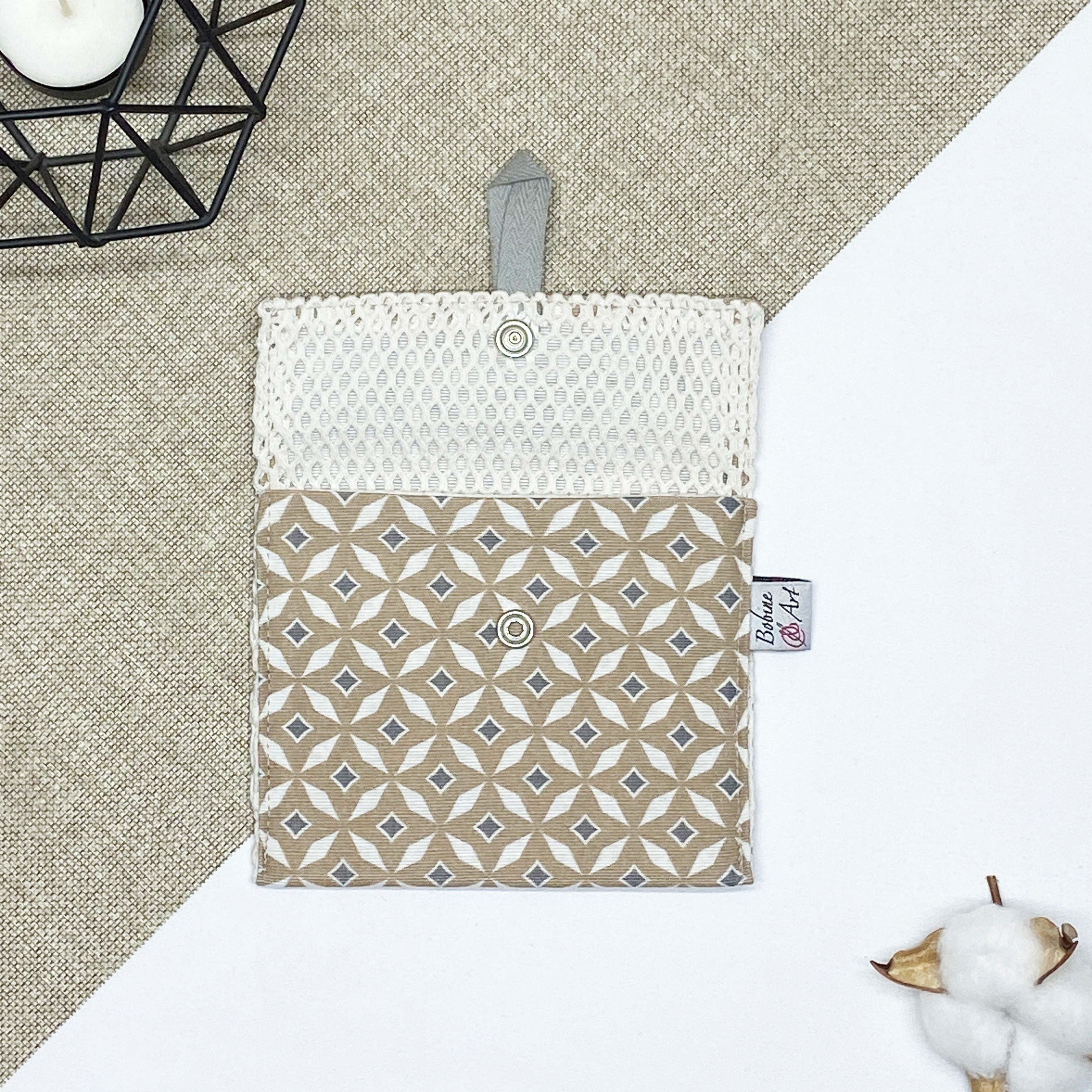 Porte-savon nomade imperméable ouvert avec filet respirant et motif géométrique beige et écru, idéal pour transporter, faire sécher et conserver un savon solide lors des déplacements et voyages.