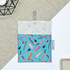 Porte-savon nomade imperméable ouvert avec filet respirant et motif maquillage composé de rouges à lèvres, pinceaux et crayons sur fond bleu turquoise, idéal pour transporter et faire sécher un savon solide en voyage.