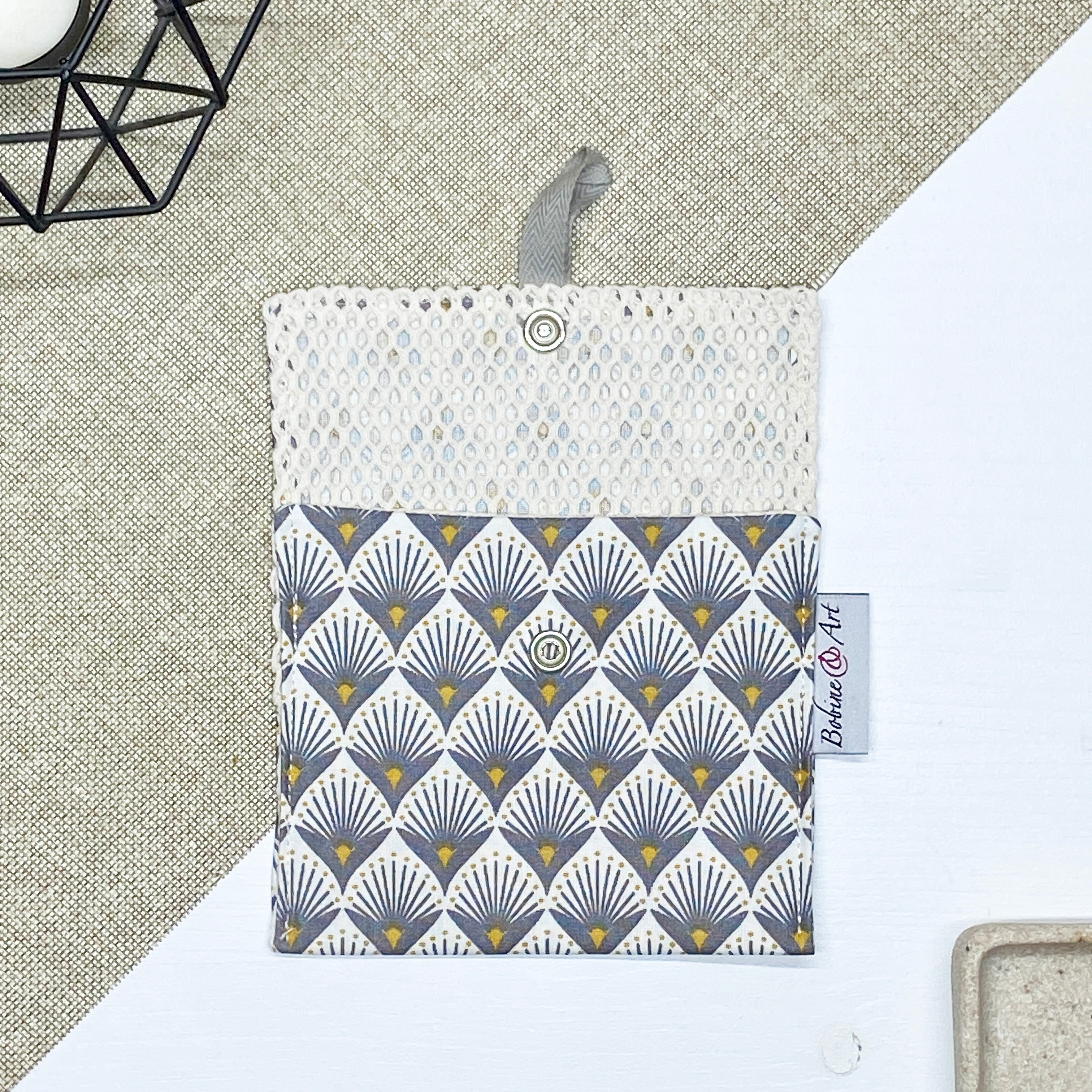 Porte-savon nomade imperméable ouvert avec filet respirant et motif éventails Art déco gris et jaune moutarde sur fond écru, idéal pour transporter, faire sécher et conserver un savon solide lors des déplacements et voyages.