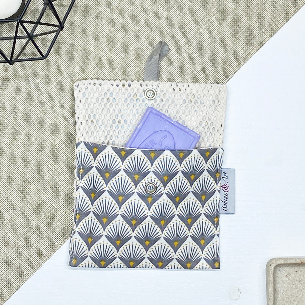 Porte-savon nomade imperméable à motif éventails Art déco gris et jaune moutarde sur fond écru, avec filet respirant et savon solide, idéal pour transporter, faire sécher et conserver un savon solide lors des déplacements et voyages.