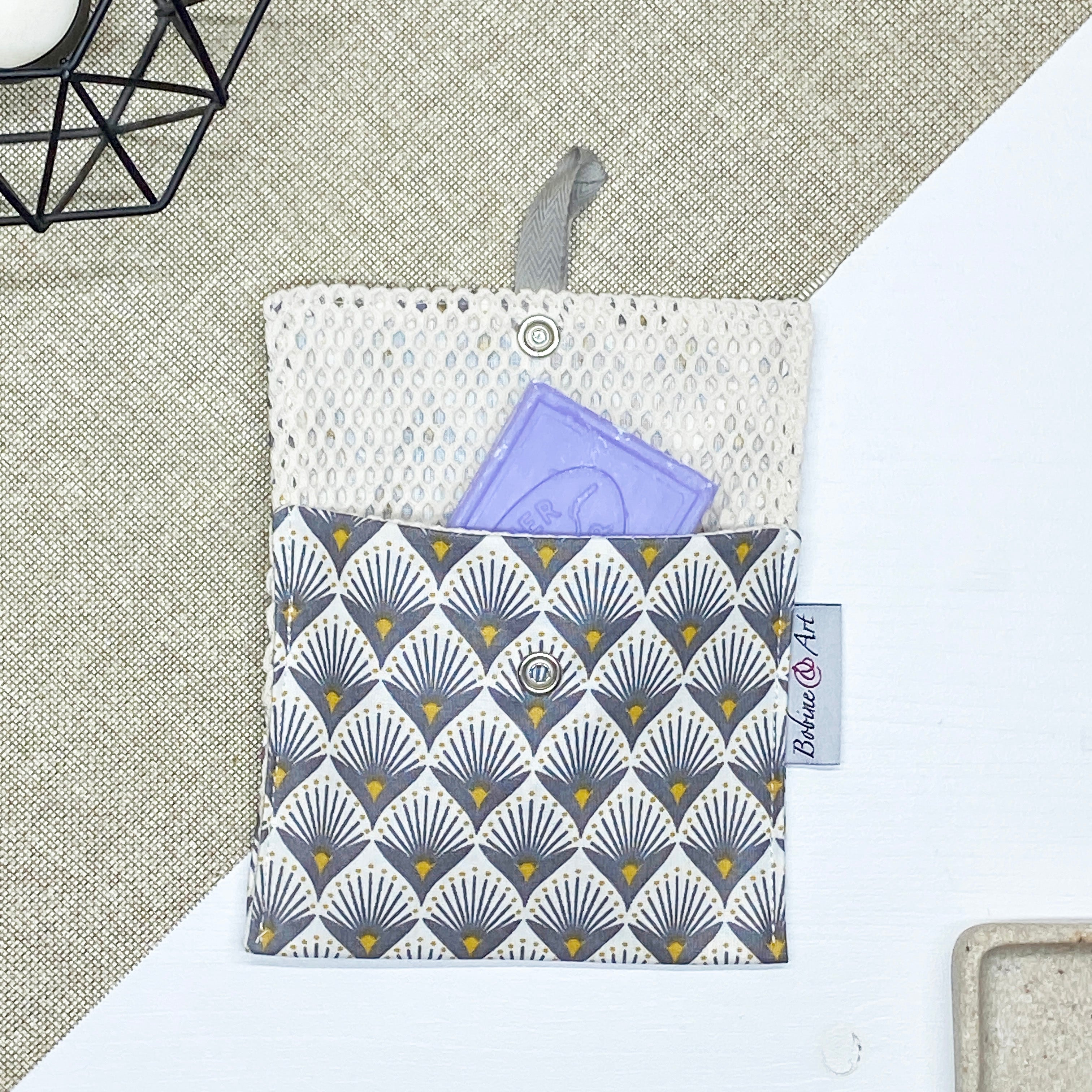 Porte-savon nomade imperméable à motif éventails Art déco gris et jaune moutarde sur fond écru, avec filet respirant et savon solide, idéal pour transporter, faire sécher et conserver un savon solide lors des déplacements et voyages.