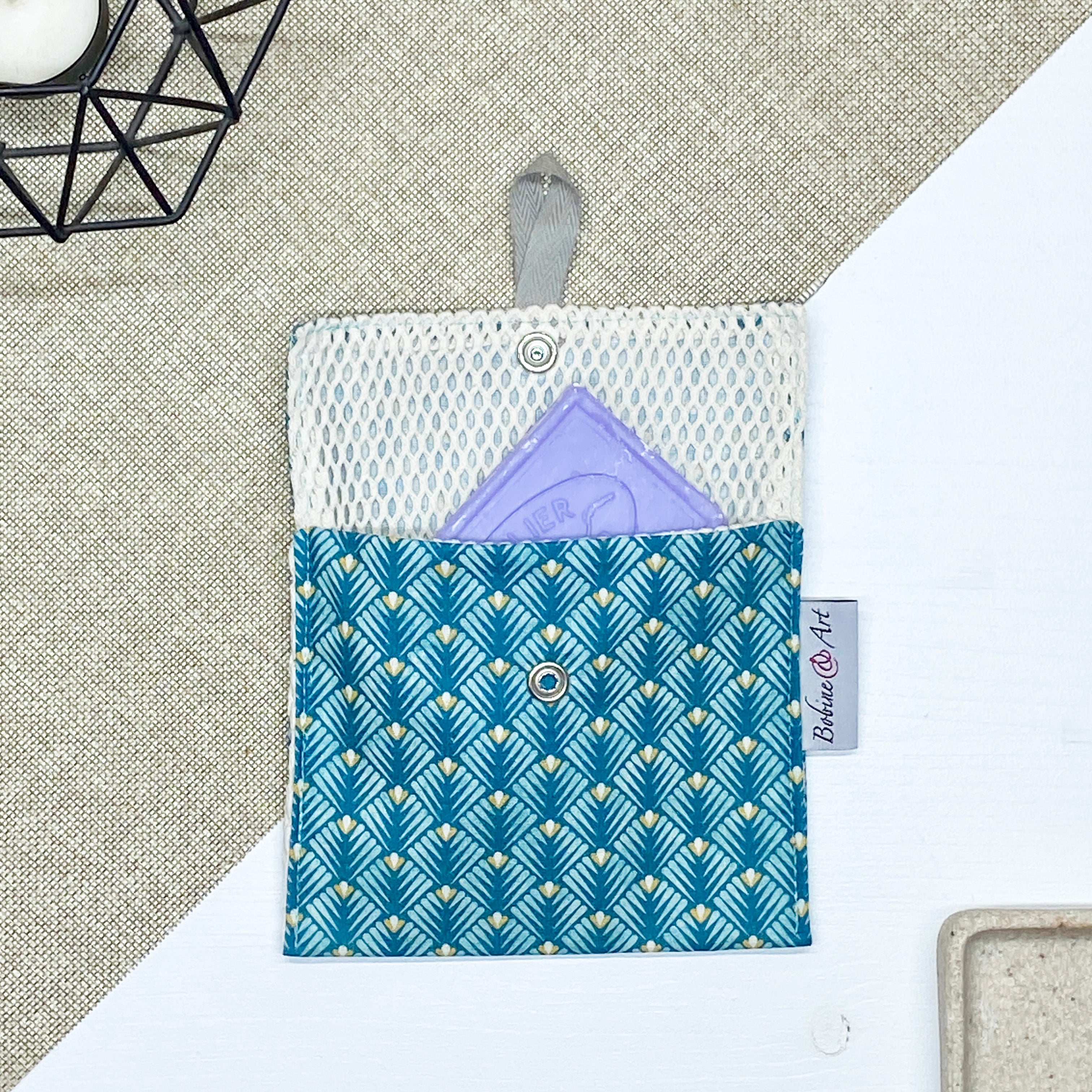 Porte-savon nomade imperméable à motif éventails géométriques bleu canard, vert d’eau et beige avec filet respirant et savon solide, idéal pour transporter, faire sécher et conserver un savon solide lors des déplacements et voyages.