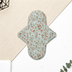 Serviette hygiénique lavable flux normal à motif fleurs sauvages, feuillages et champignons sur fond bleu grisé, protection périodique réutilisable à forte absorption adaptée aux flux normaux.