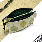 Trousse de toilette artisanale ouverte en tissu avec motif feuilles rondes vertes, double compartiment et intérieur imperméable.