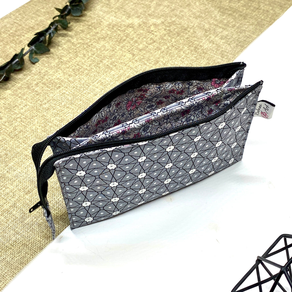 Trousse de toilette artisanale ouverte en tissu avec motif géométrique gris et blanc, double compartiment et intérieur imperméable.